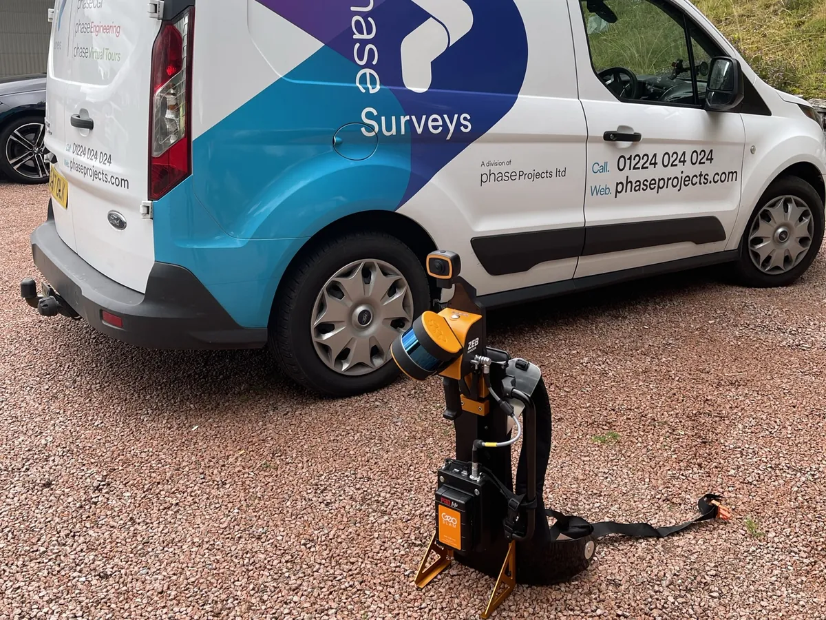 A GeoSLAM handheld scanner standing on the ground beside the Phase Surveys van