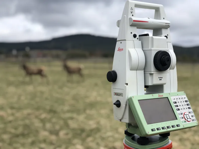 A total station in a field with deer grazing behind it